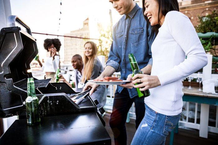 A group of people serve themselves from an outdoor grill.